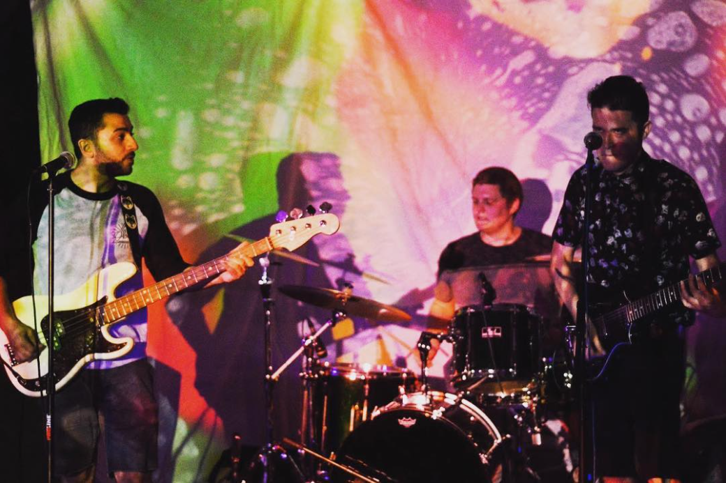 The band Townsville performing live against a psychedelic multicolored curtain backdrop.